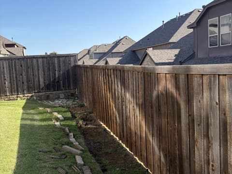 Stone border and new plantings running along a backyard cedar fence