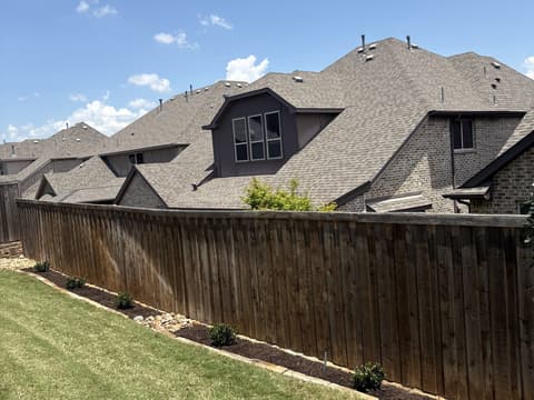 River-rock bordered beds with young shrubs along a wooden fence