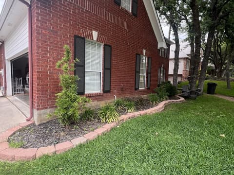 Crisp flower bed edge with dark mulch curving along a red brick house