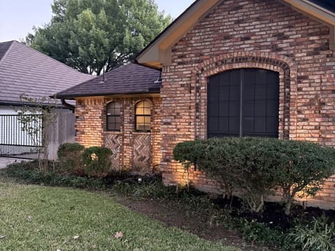 Brick home at dusk with freshly mulched beds and landscape lighting