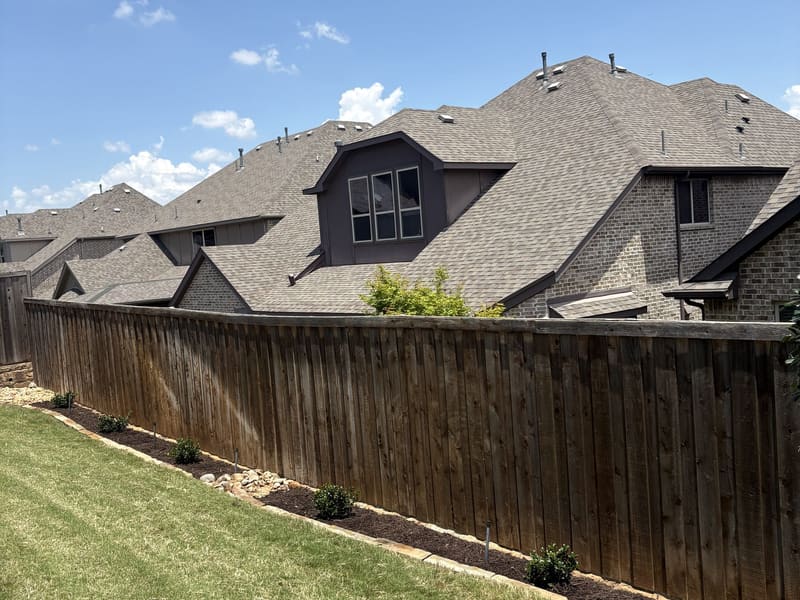 Stone-bordered landscape beds installed along a backyard cedar fence
